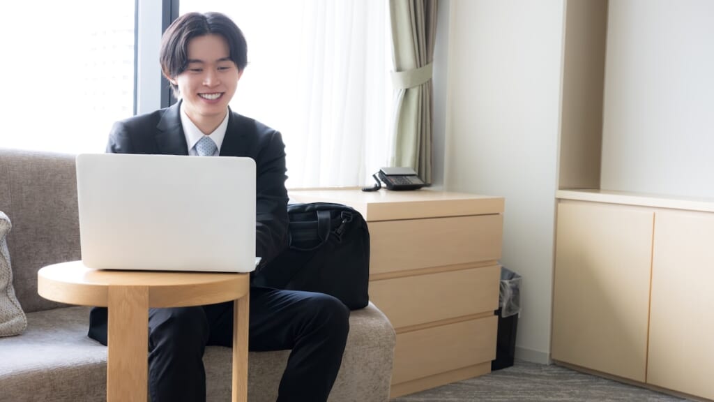 出張先のホテルでPCを開く笑顔の男性